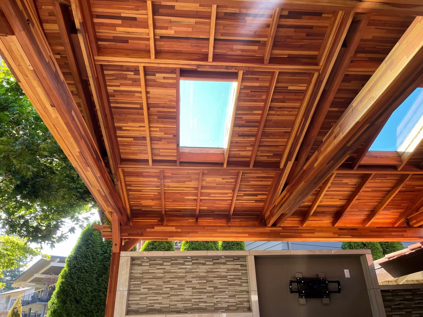 Underside of a cedar pavilion roof with exposed beams and two skylights, above a tiled outdoor wall