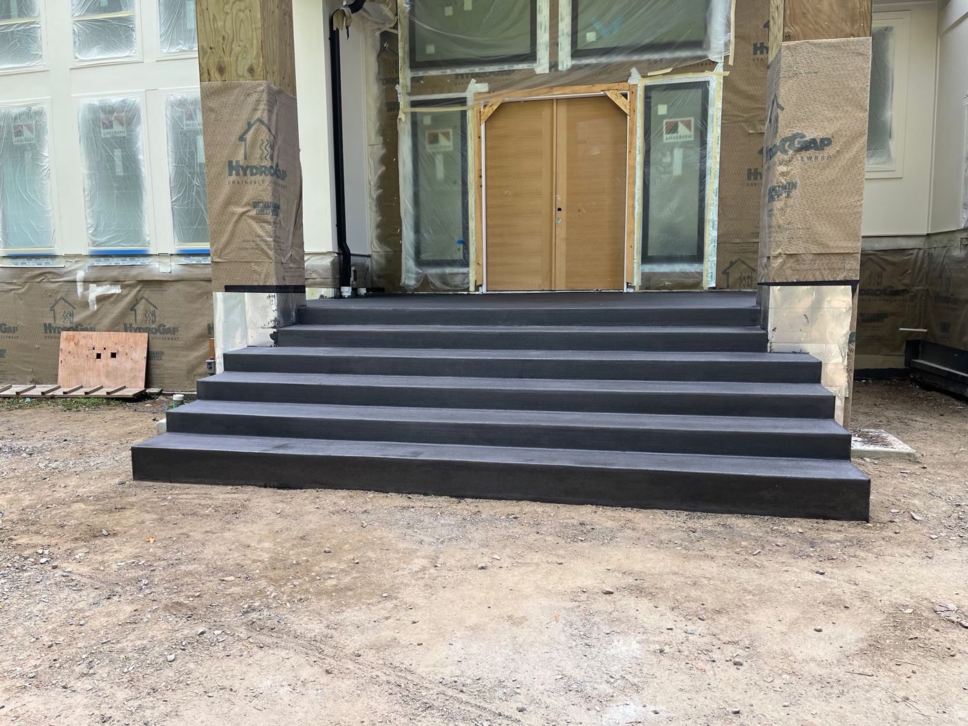 Wide charcoal-colored concrete front entry stairs leading up to double doors on a new home under construction