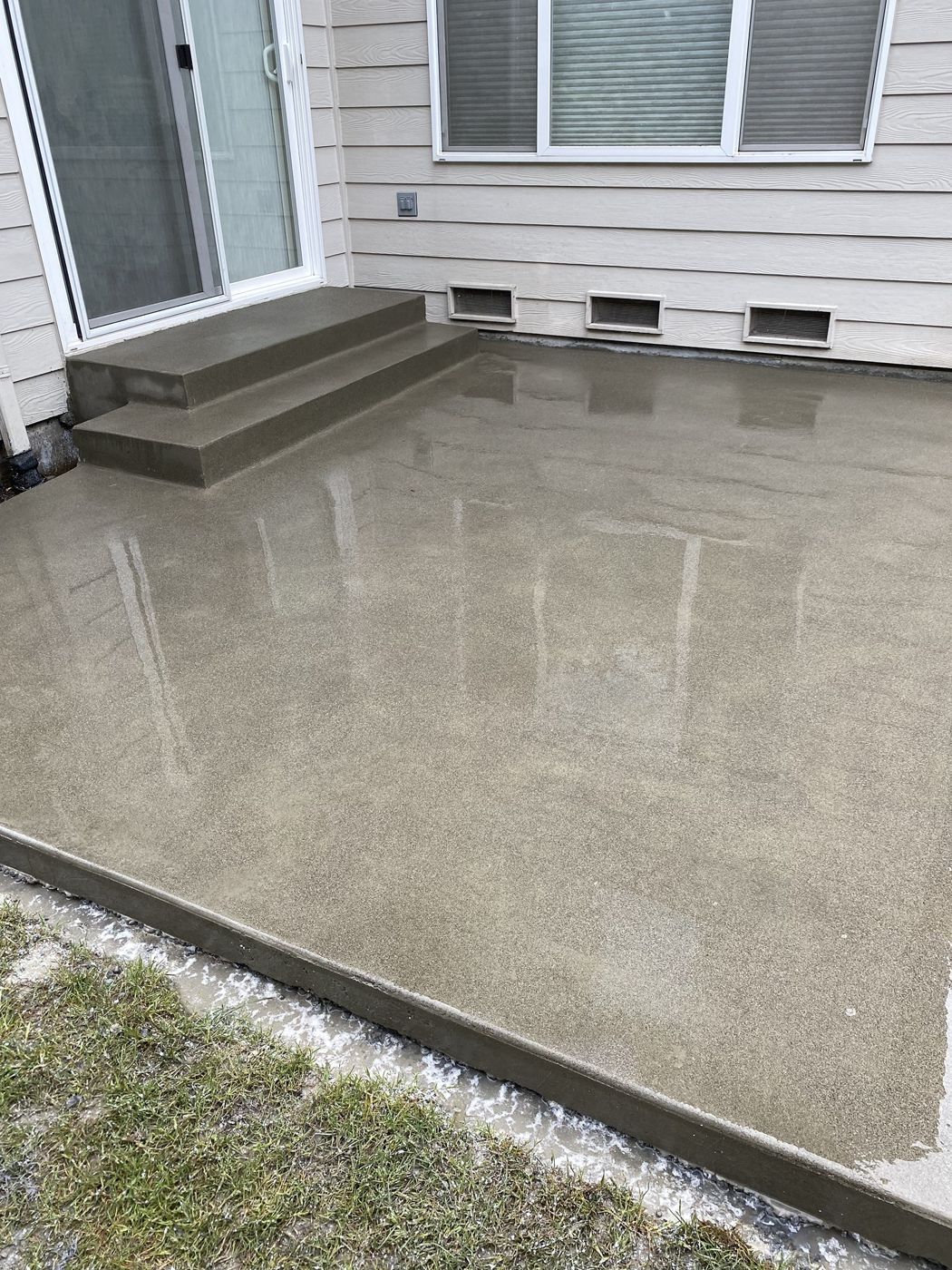 Freshly poured concrete patio with two wide steps up to a sliding door