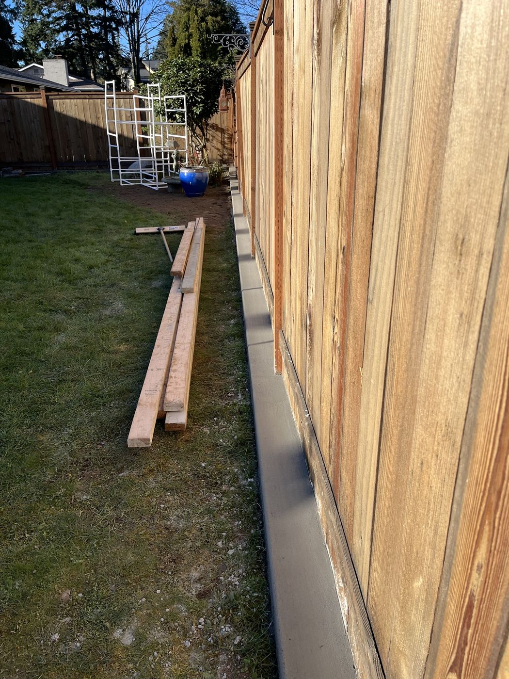 Narrow concrete mow strip poured along the base of a wood fence