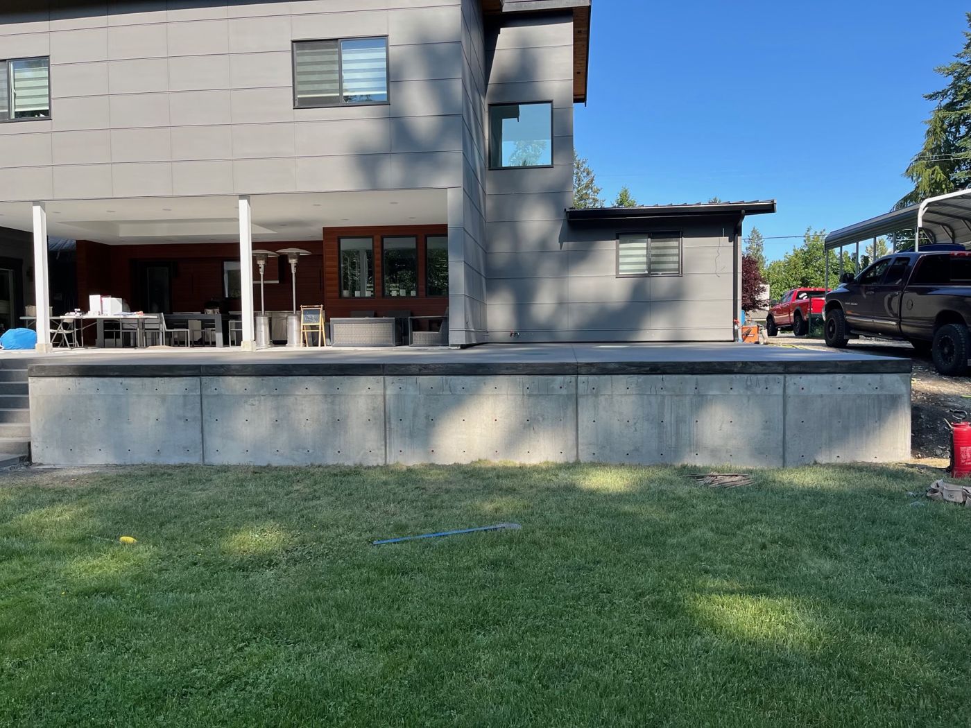 Large raised concrete patio on a board-formed retaining wall behind a modern home, extending a covered outdoor living area