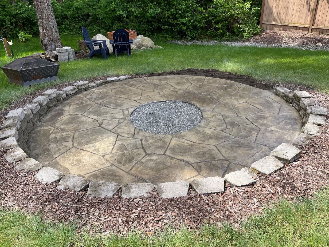 Round stamped flagstone concrete patio with a gravel fire-pit center, edged with stone blocks