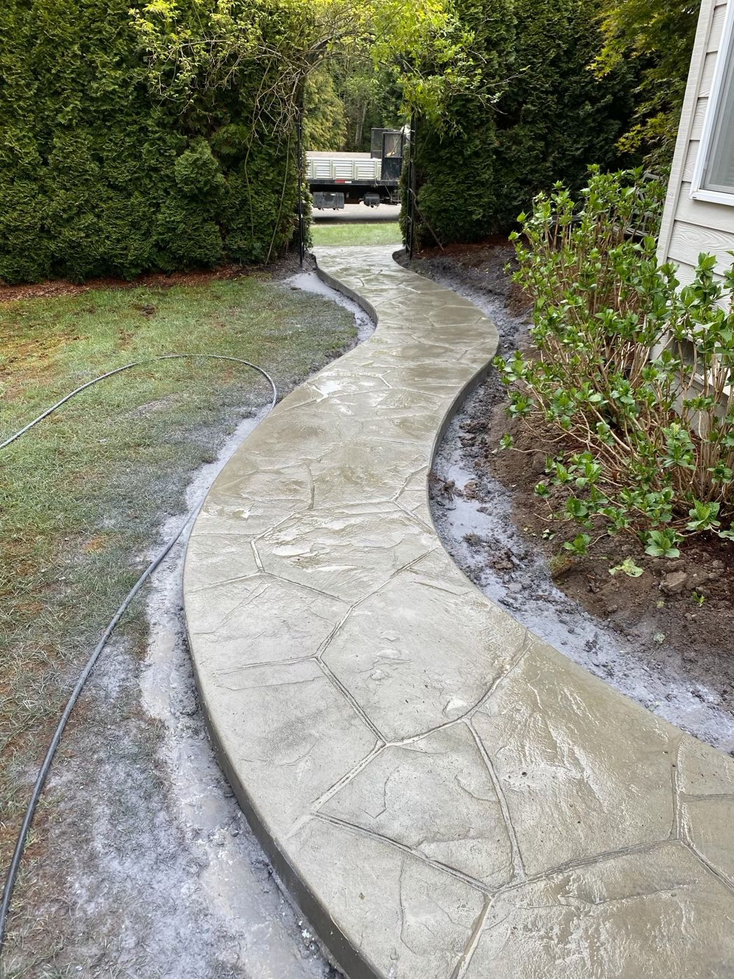 Curving concrete walkway stamped with a flagstone pattern, leading through a hedge archway