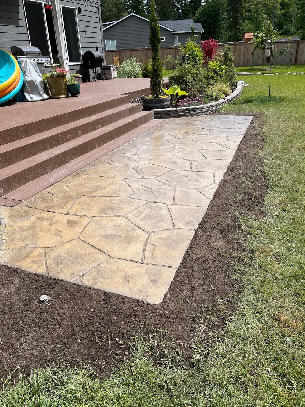 Tan stamped flagstone concrete patio at the base of wide deck stairs