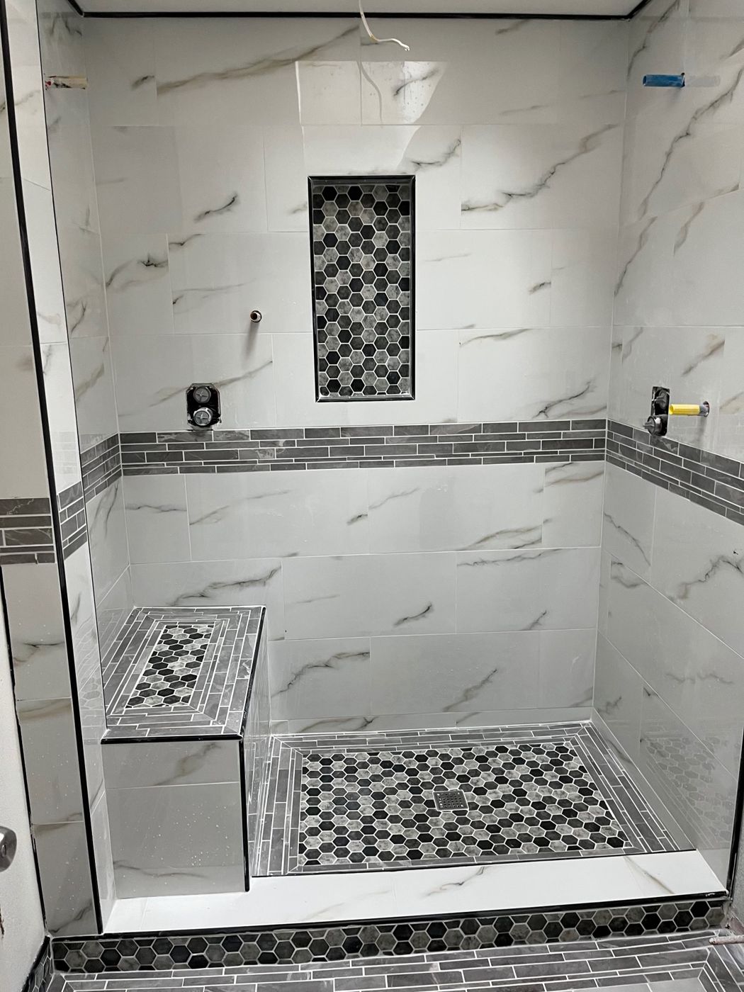 Walk-in shower with marble-look wall tile, a hexagon mosaic floor, built-in bench and recessed niche