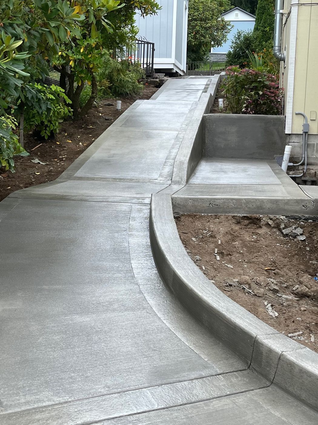 Concrete walkway with a curved curb, low wall and landing beside a house